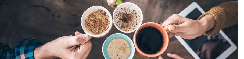 Vier Hände stoßen Tassen mit verschiedenen Kaffees an
